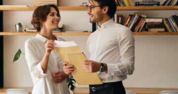 Young attractive business colleagues standing with envelope letter happily looking at each other in modern office