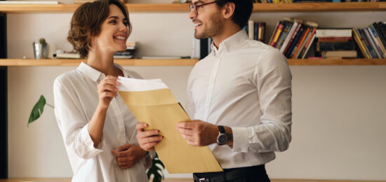 Young attractive business colleagues standing with envelope letter happily looking at each other in modern office