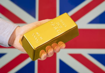 The gold reserve of the Great Britain concept. Gold bar in hand on Britain flag background
